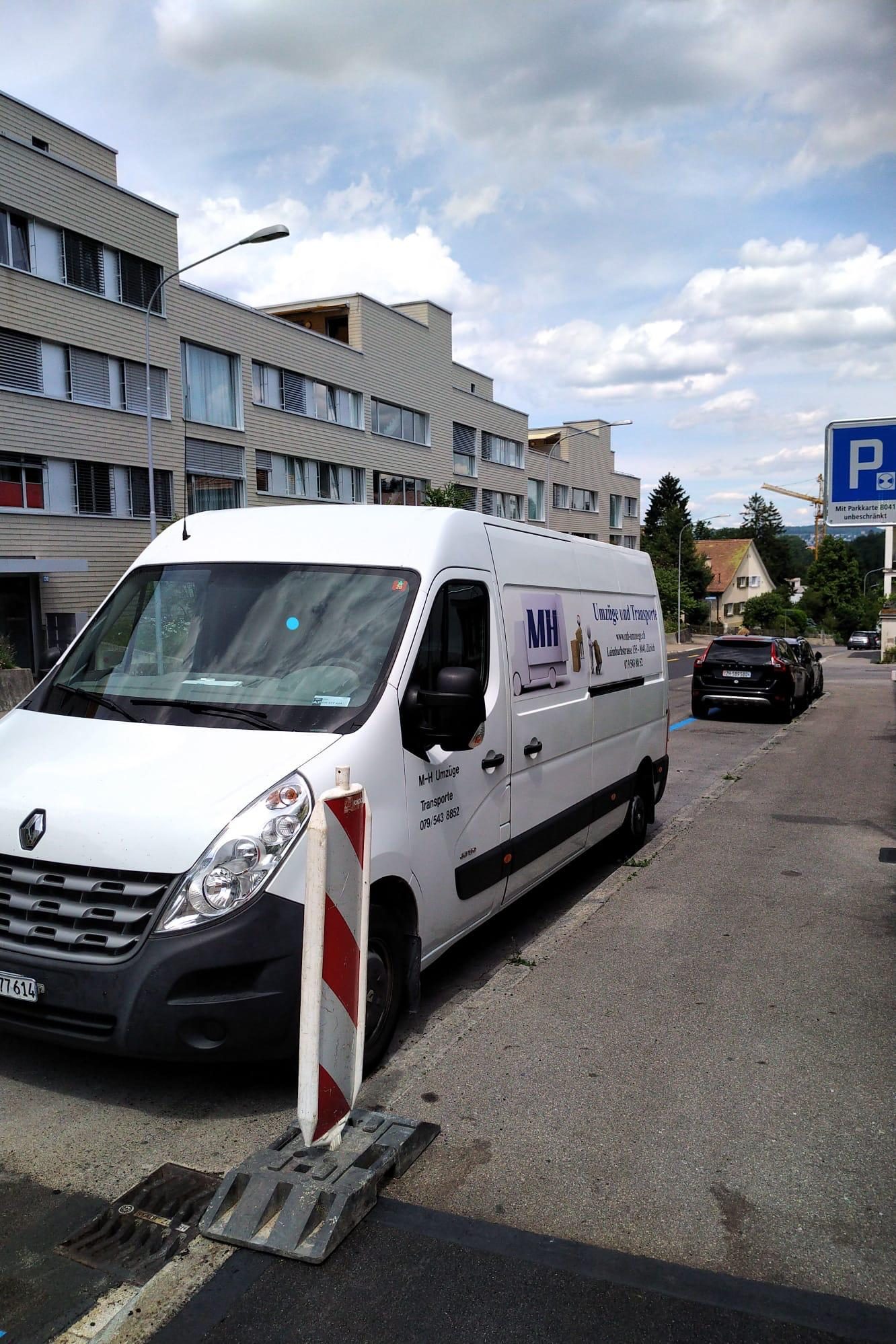 Weisser MH-Lieferwagen mit Firmenlogo in einer Zürcher Strasse neben einem Verkehrskegel