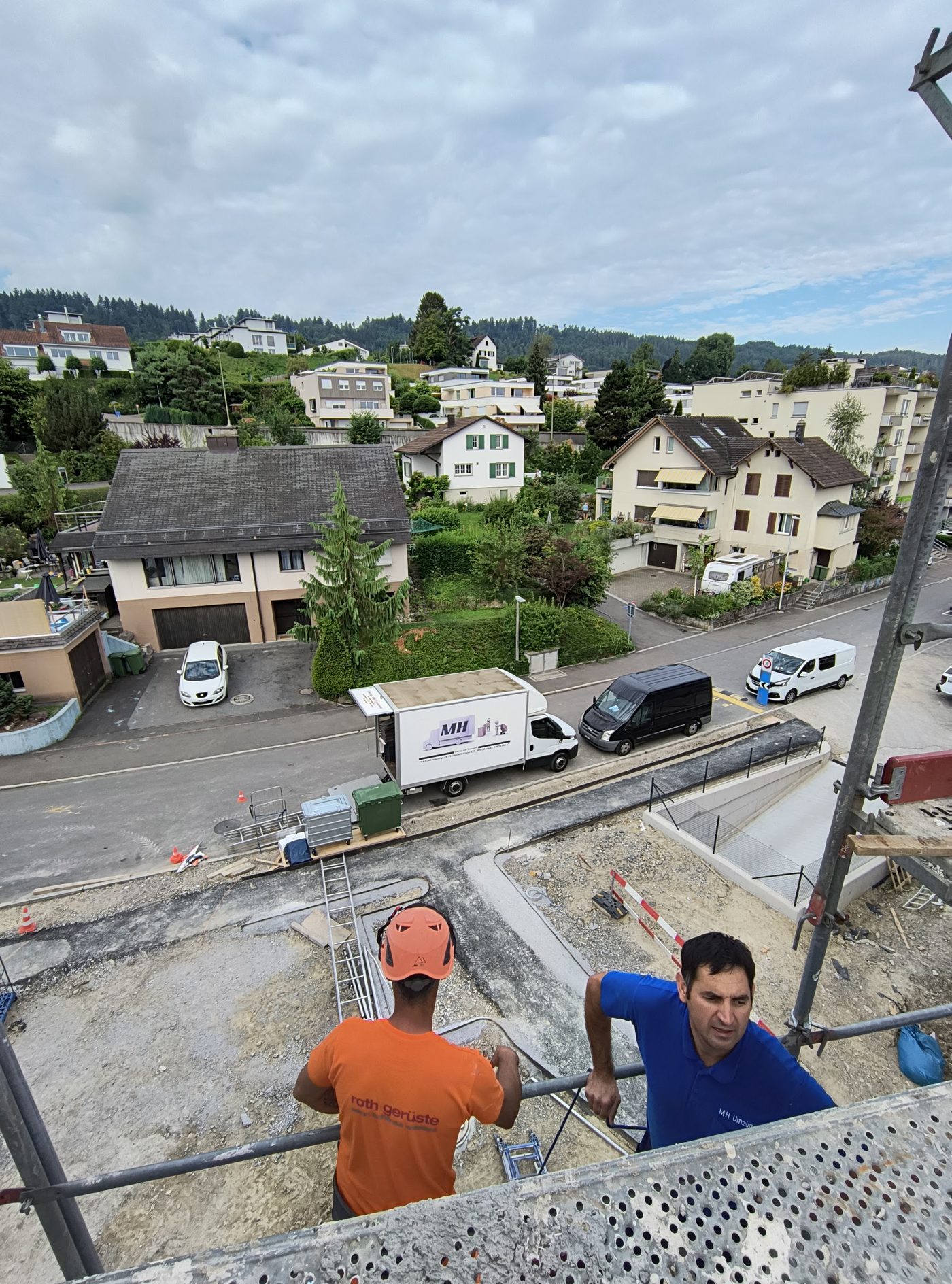 Zwei Mitarbeiter auf der Plattform des Möbellifts über einer Wohnstrasse, unten der Lastwagen